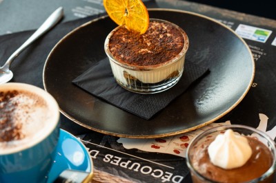 Desserts variés sur une table, incluant un tiramisu décoré d'une tranche d'orange, une mousse au chocolat et un cappuccino.