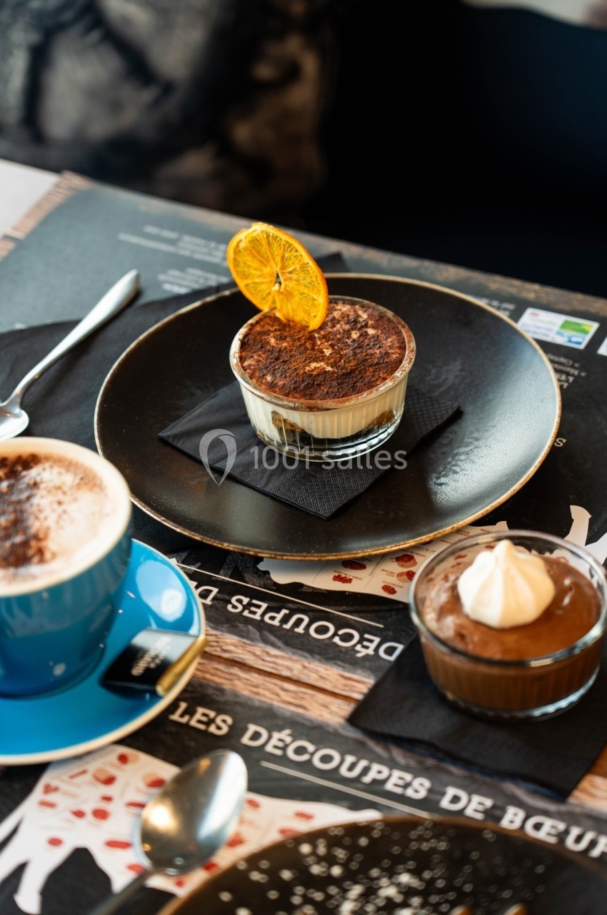 Desserts variés sur une table, incluant un tiramisu décoré d'une tranche d'orange, une mousse au chocolat et un cappuccino.