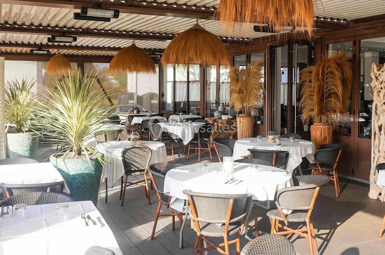 Salle de restaurant avec tables dressées en extérieur, décorée de plantes et suspensions en fibres naturelles.