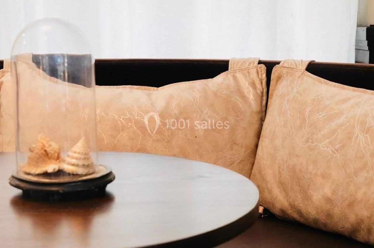 Coussins beige texturés sur une banquette en bois sombre, avec une table ronde et une cloche en verre contenant des…
