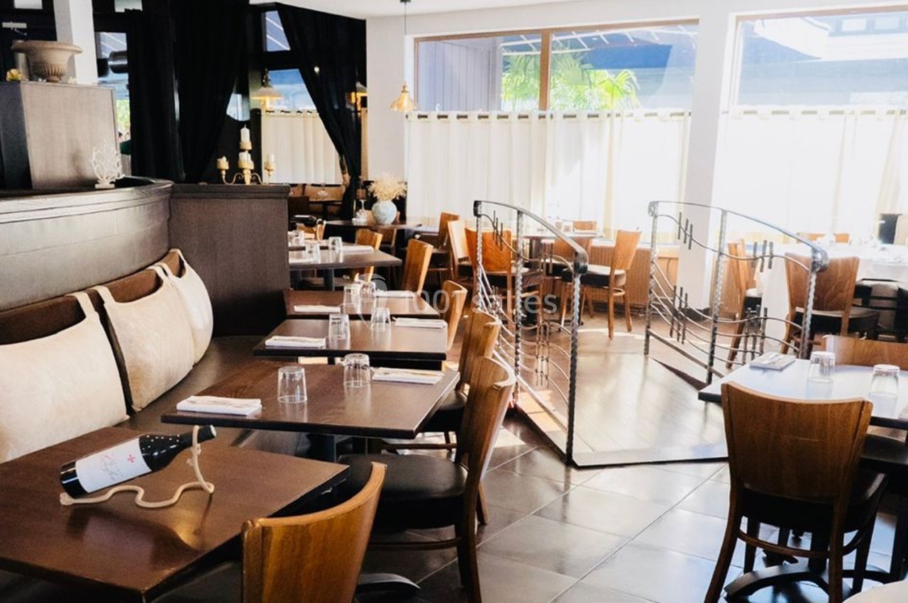 Salle de restaurant lumineuse avec tables en bois, chaises assorties et une bouteille de vin posée sur une table.
