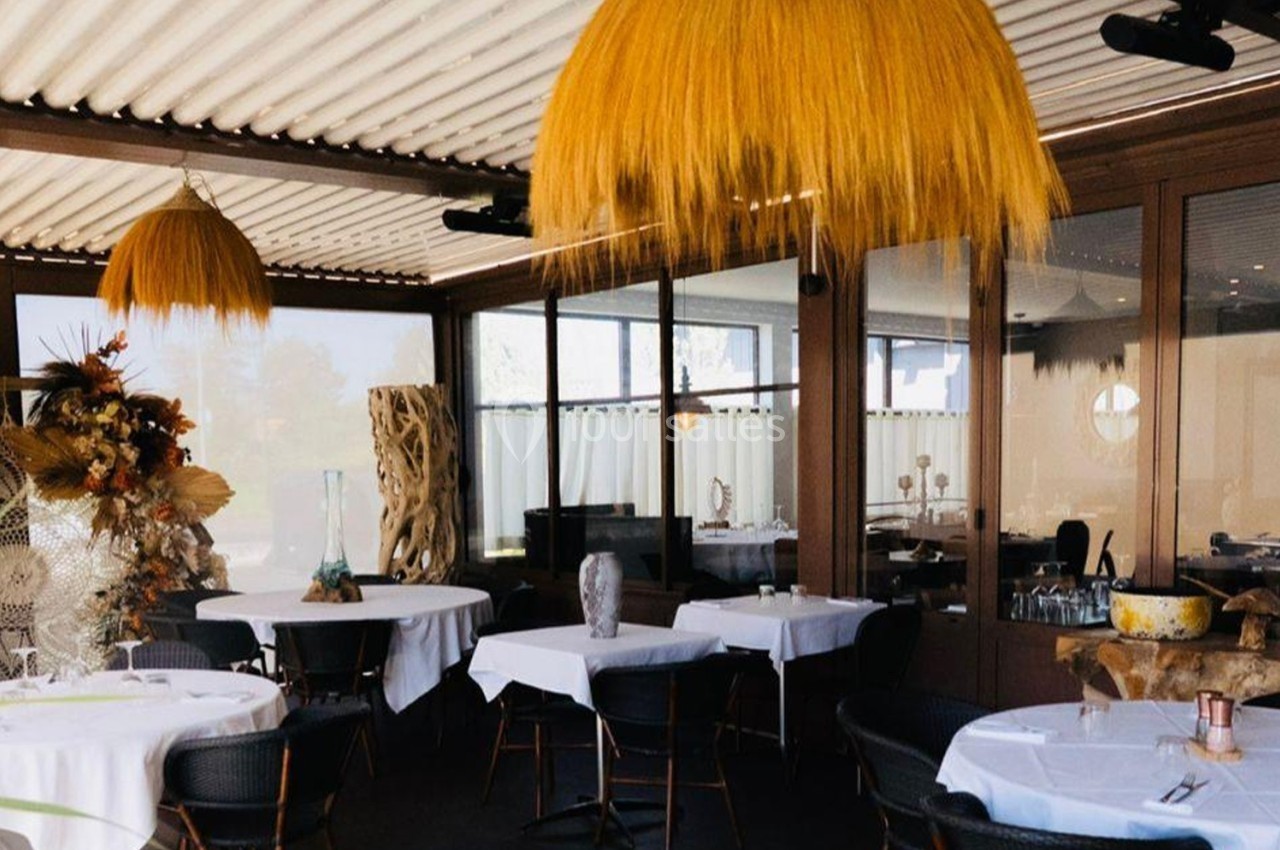 Salle de restaurant avec tables dressées, grandes suspensions en fibres naturelles et décoration végétale.