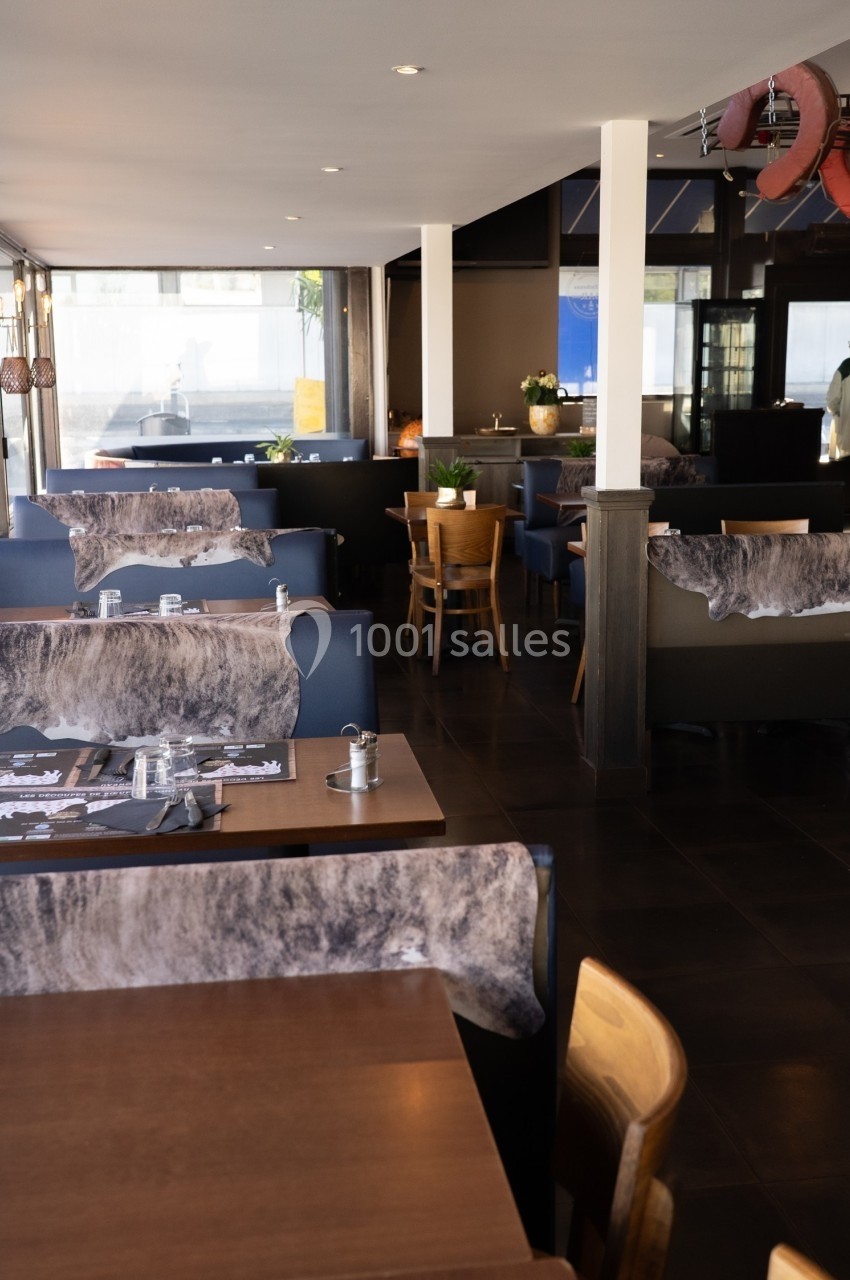 Salle de restaurant moderne avec tables en bois, chaises rembourrées et décoration sobre.