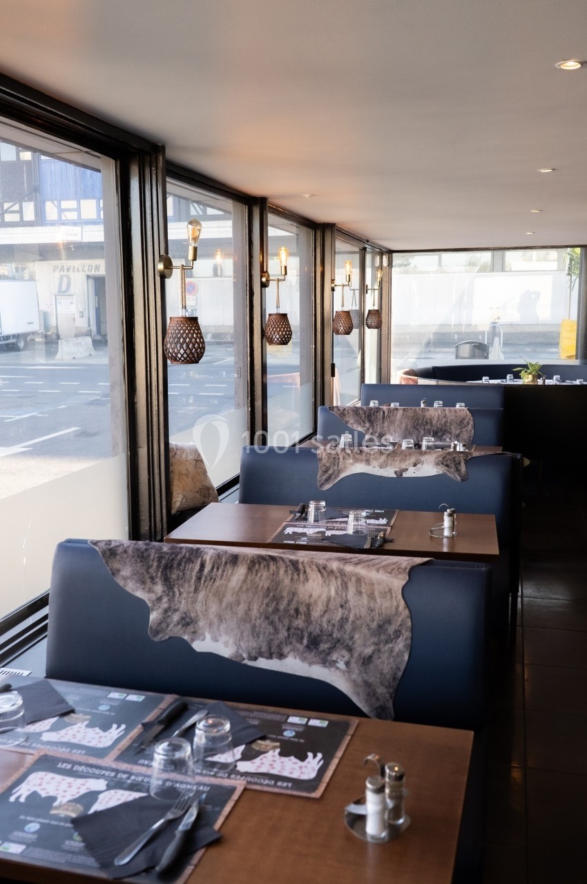 Salle de restaurant avec tables en bois, banquettes décorées de motifs animaux et grandes baies vitrées donnant sur la rue.