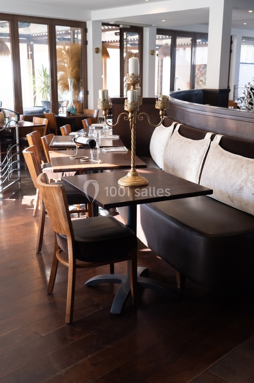 Salle de restaurant lumineuse avec tables en bois, banquettes en cuir et chandelier doré au centre.