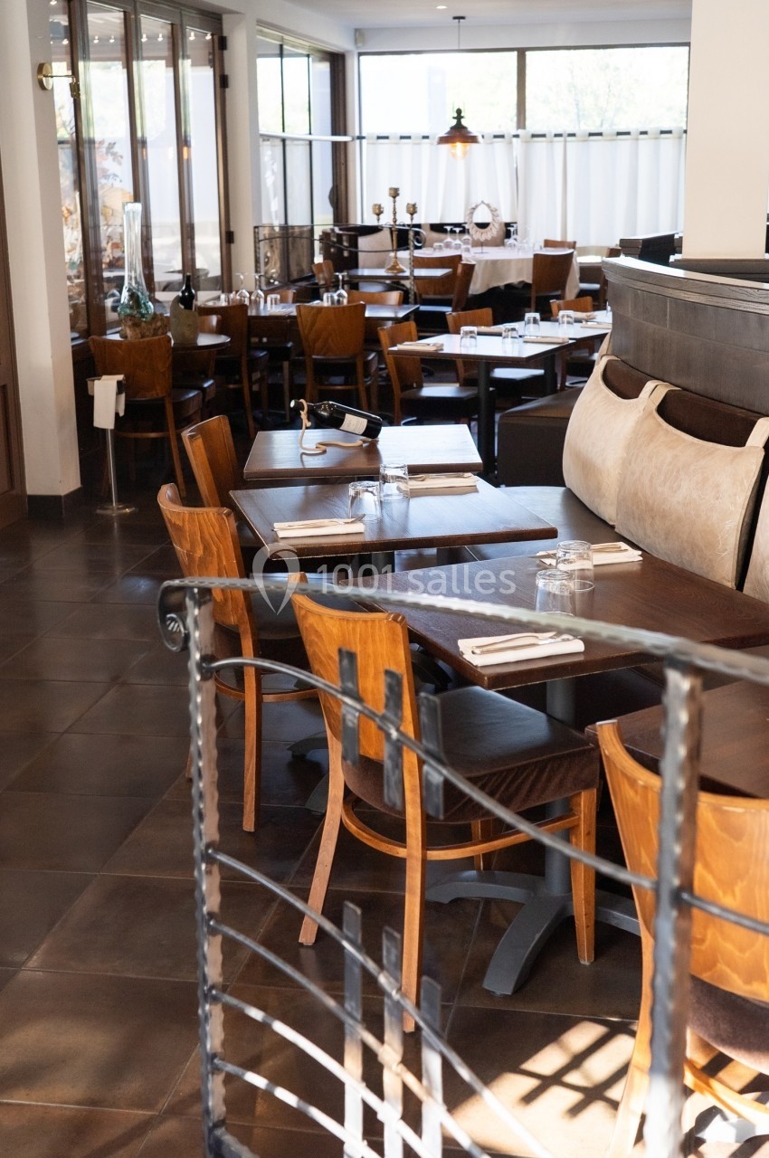 Salle de restaurant lumineuse avec tables en bois, chaises assorties et grandes baies vitrées en arrière-plan.