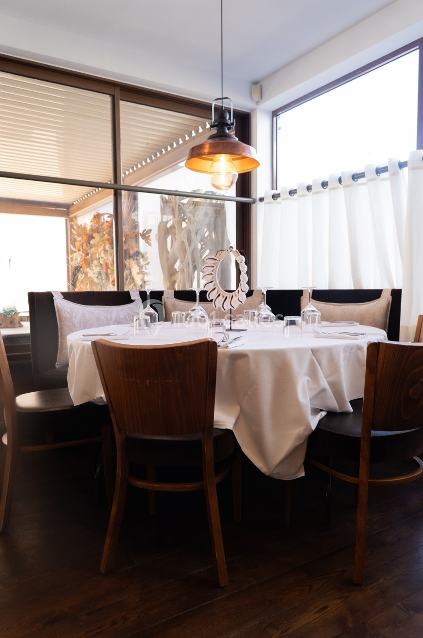Table ronde dressée avec une nappe blanche, entourée de chaises en bois, dans un restaurant lumineux.