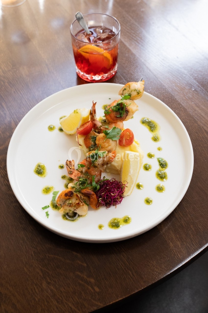 Assiette de crevettes grillées avec citron, tomates cerises, herbes fraîches et sauce, accompagnée d'un verre de cocktail.