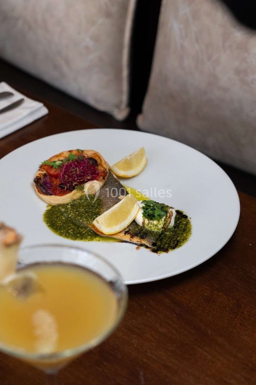 Assiette de poisson grillé avec sauce verte, légumes colorés en garniture et quartiers de citron, servie sur une table en…