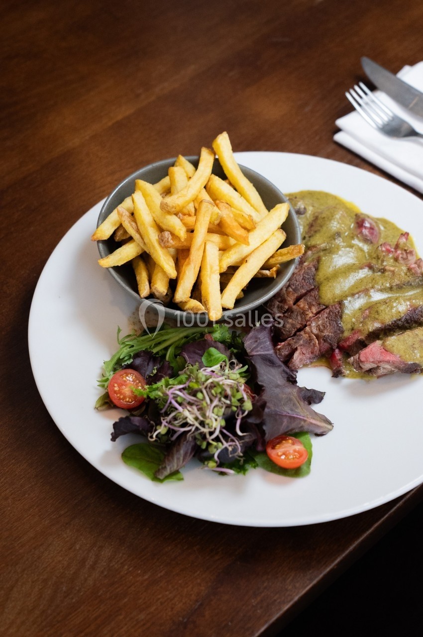 Assiette contenant une pièce de viande avec sauce, accompagnée de frites et d'une salade verte avec tomates cerises.