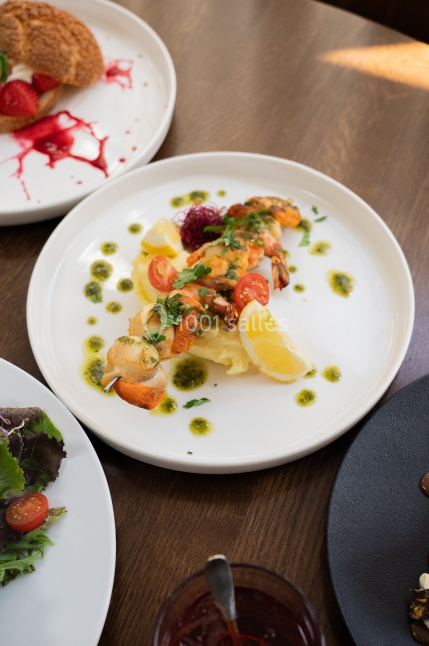 Assiette de crevettes grillées servies sur un lit de purée, décorée de citron, herbes fraîches et sauce verte.