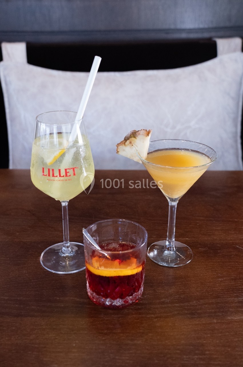 Trois cocktails variés sur une table en bois, comprenant un verre de Lillet, un cocktail au martini et un verre de Negroni.
