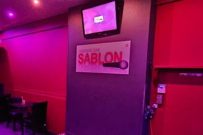 Miniature Location salle Bruxelles (Bruxelles-Capitale) - Karaoke Bar Sablon #7 Écran et panneau indiquant ’Karaoké Bar Sablon’ avec un micro, dans une salle éclairée par des lumières violettes.