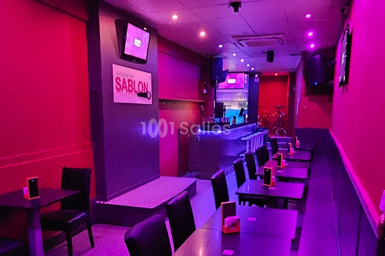 Salle de restaurant ou bar avec éclairage rose, tables alignées et comptoir lumineux au fond.