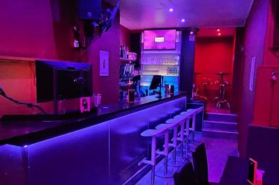 Scène de karaoké dans un bar avec éclairage rose et rouge, micro illustré sur un panneau mural.