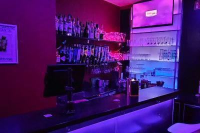 Scène de karaoké dans un bar avec éclairage rose et rouge, micro illustré sur un panneau mural.