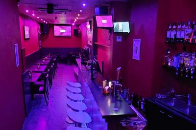 Scène de karaoké dans un bar avec éclairage rose et rouge, micro illustré sur un panneau mural.