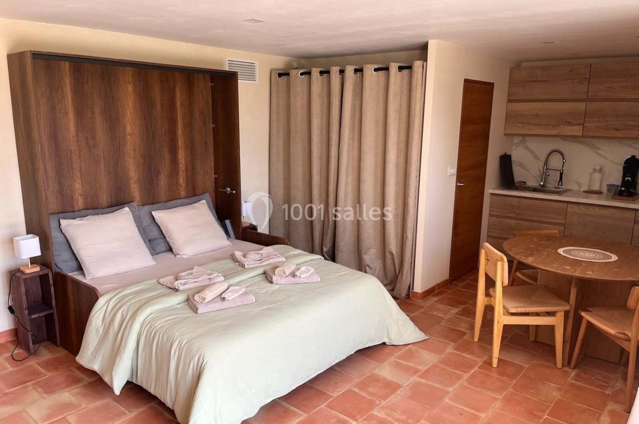 Chambre avec lit double, kitchenette équipée, table ronde en bois et sol en carrelage terracotta.