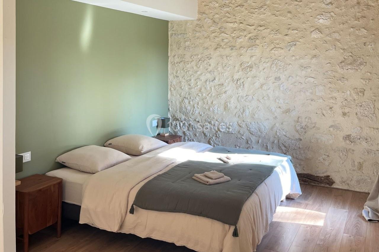 Chambre lumineuse avec un lit double, mur en pierre apparente, mur vert et sol en bois clair.