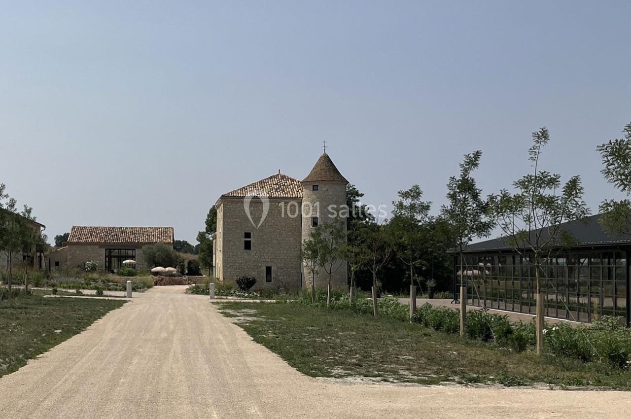 Chemin en gravier menant à un bâtiment en pierre avec une tour, entouré d'arbres et d'espaces verts.