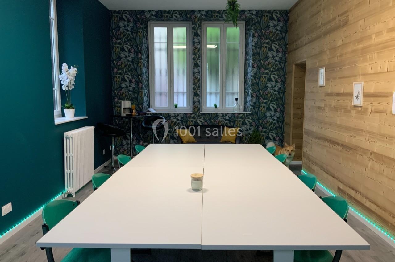 Salle de réunion avec une grande table blanche, chaises vertes, mur en bois et décoration végétale.