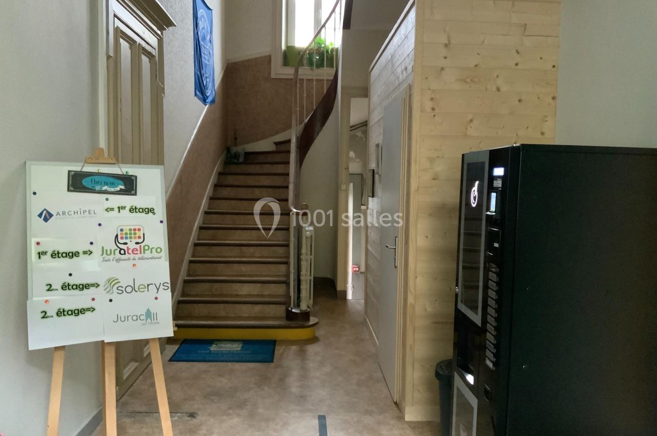 Entrée d'un bâtiment avec un escalier, un panneau indiquant des entreprises et un distributeur automatique à droite.