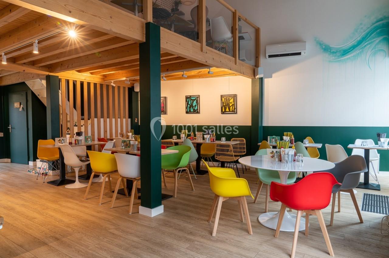 Salle de restaurant moderne avec des tables rondes, des chaises colorées et une mezzanine en bois.