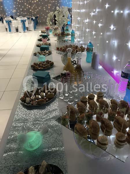 Buffet de réception avec verrines, sandwichs et boissons, disposé sur une table décorée de lumières et nappes élégantes.
