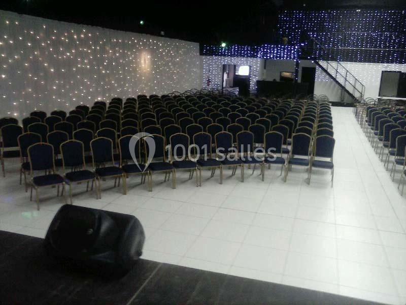 Salle de conférence avec des rangées de chaises vides, éclairée par des lumières décoratives sur les murs.