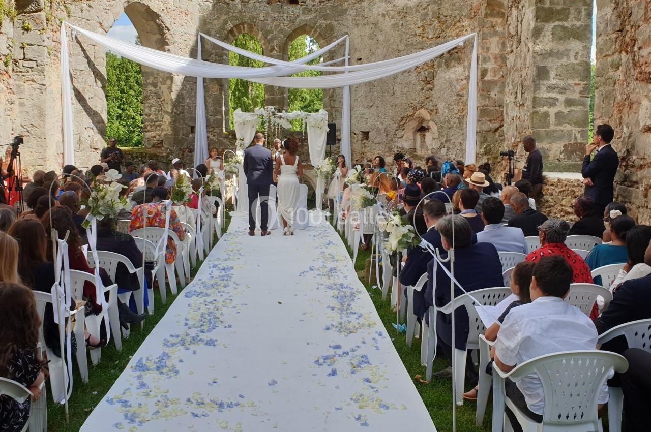 Cérémonie de mariage en plein air dans une ruine historique, avec des invités assis et un couple devant l'autel.