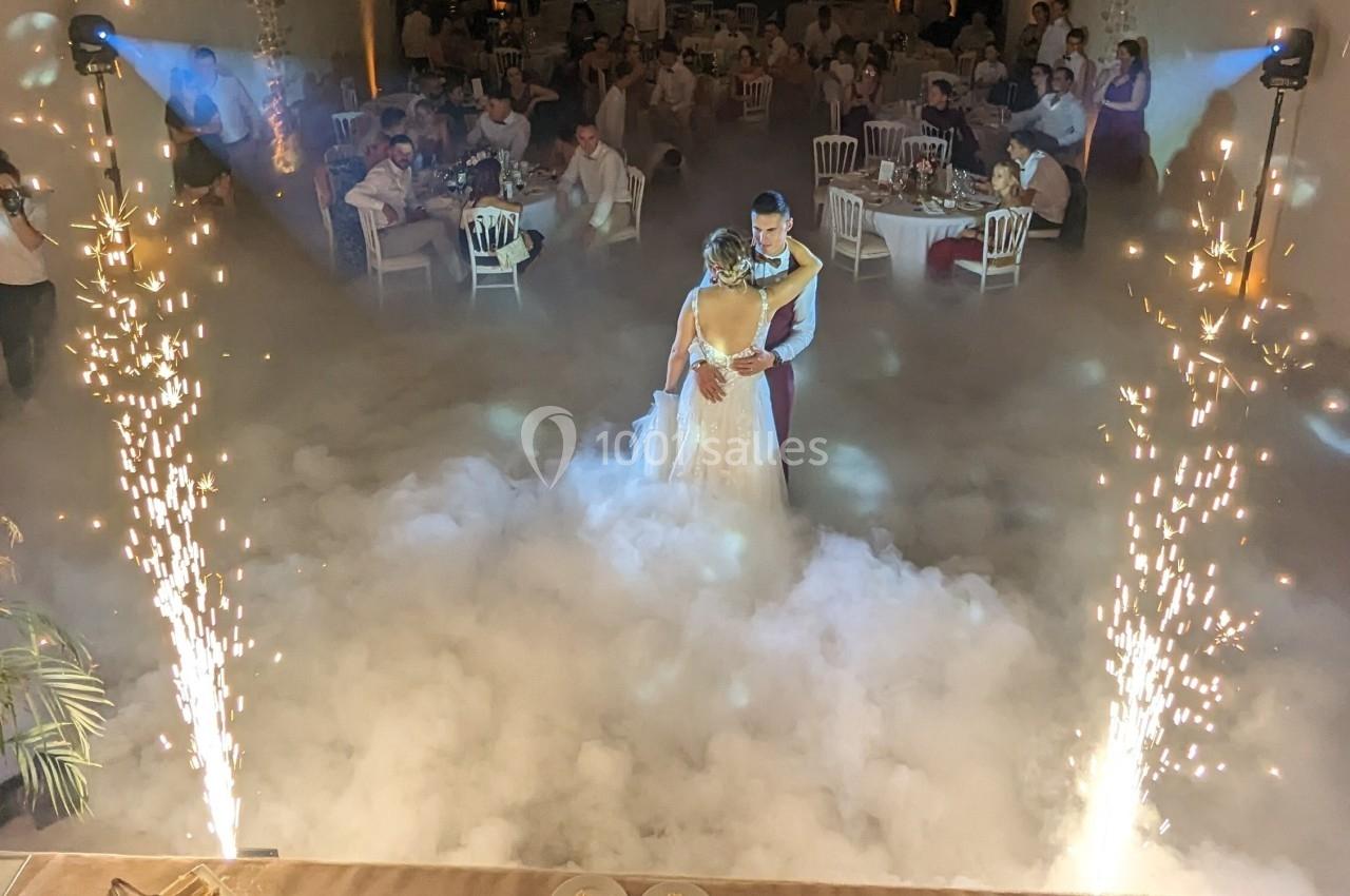 Un couple danse au milieu d'une piste entourée de fumée et d'effets pyrotechniques, sous le regard des invités.