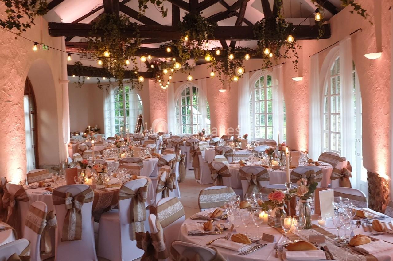 Salle de réception décorée avec des guirlandes lumineuses, des tables dressées et des chaises ornées de rubans.