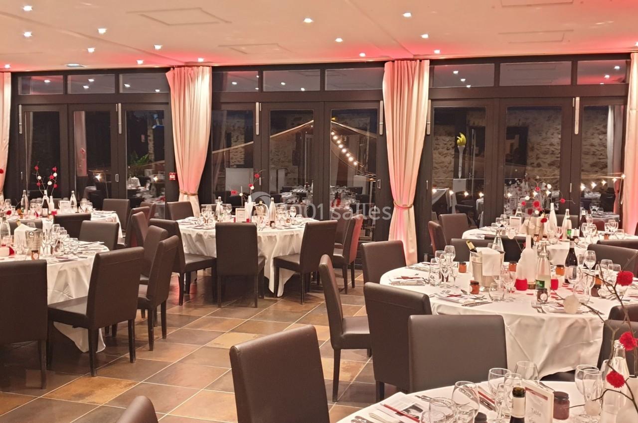Salle de réception élégante avec tables rondes dressées, nappes blanches et décorations florales rouges.