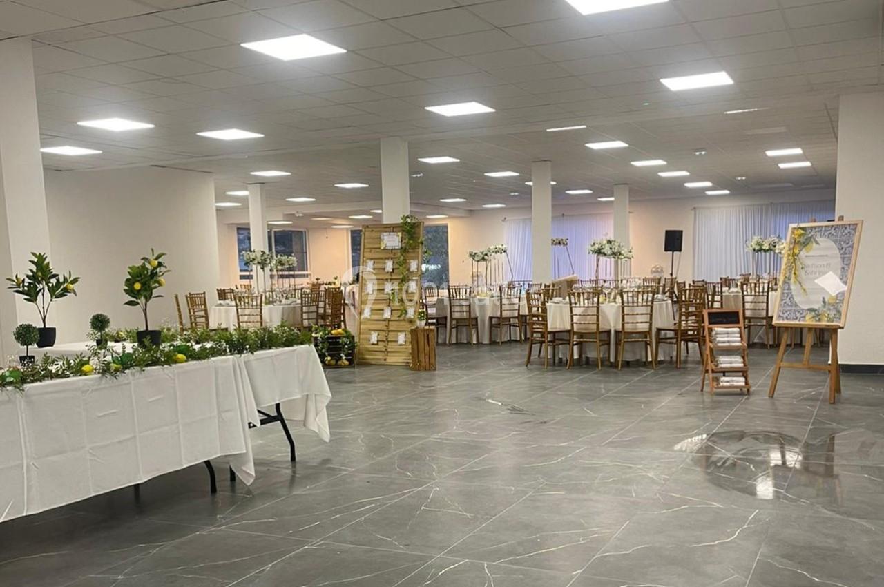 Salle de réception lumineuse avec tables dressées, décoration florale et espace aménagé pour un événement.