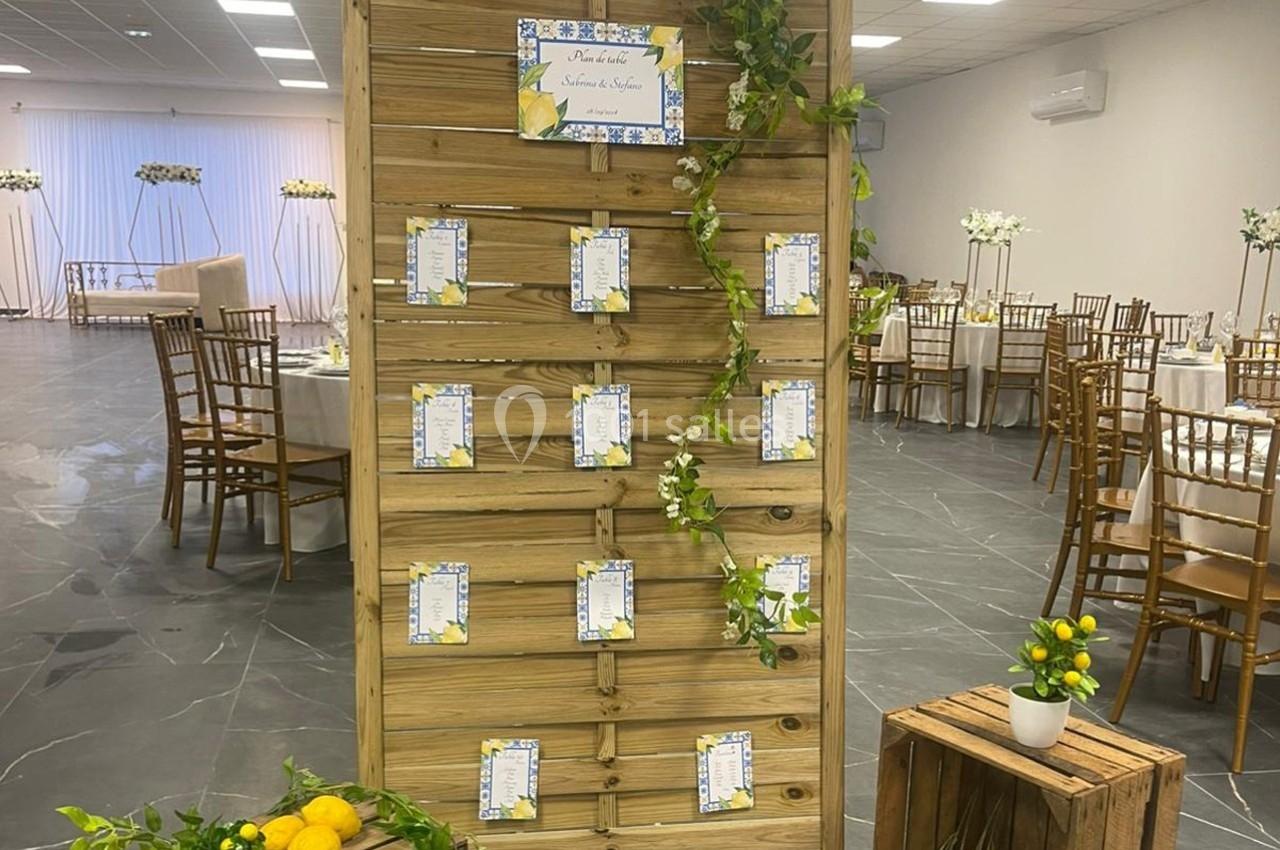 Panneau en bois décoré de feuillage, affichant des cartes de placement, dans une salle de réception élégamment aménagée.