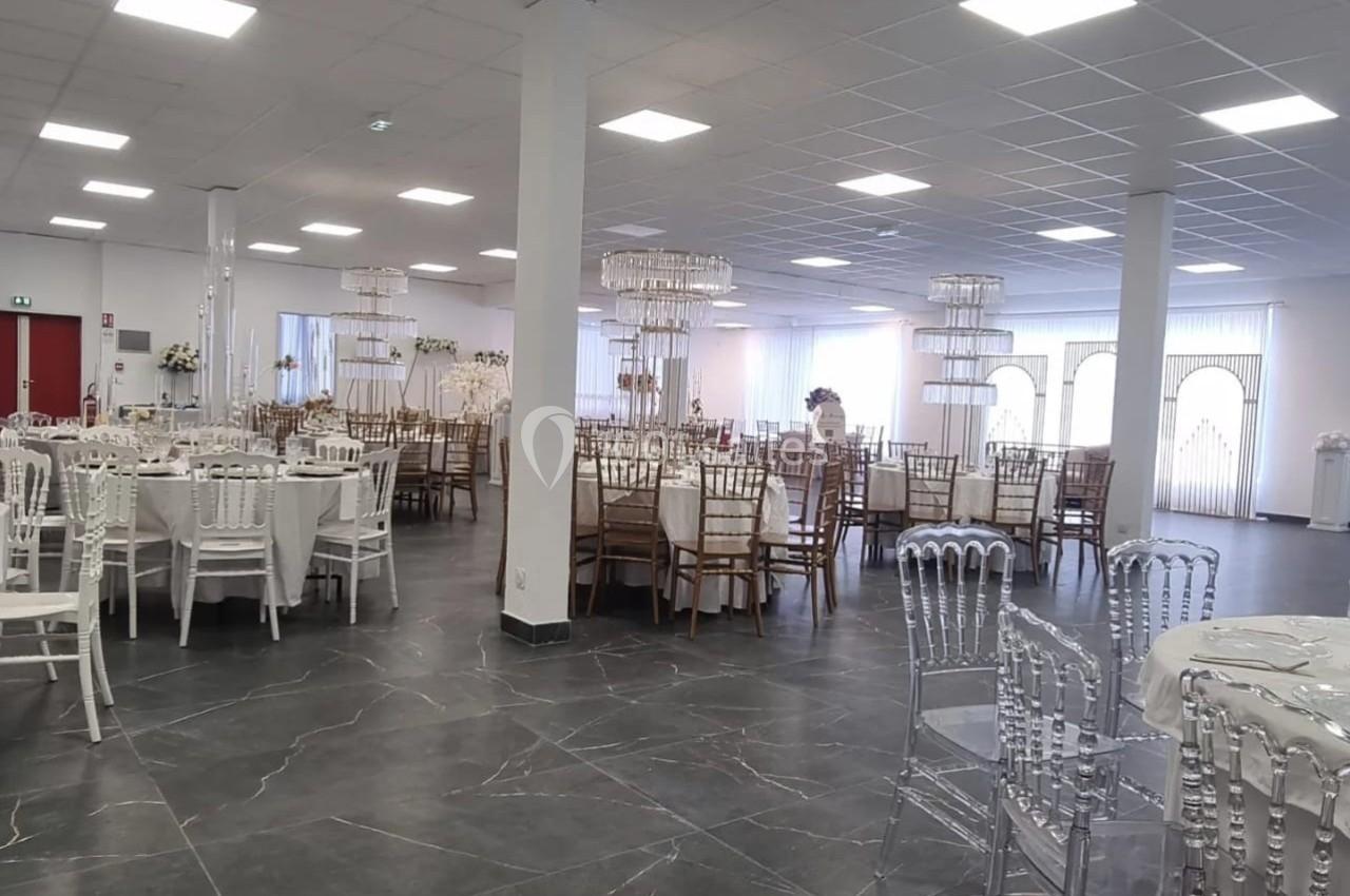 Salle de réception lumineuse avec tables dressées, chaises variées et décorations élégantes dans un espace spacieux.