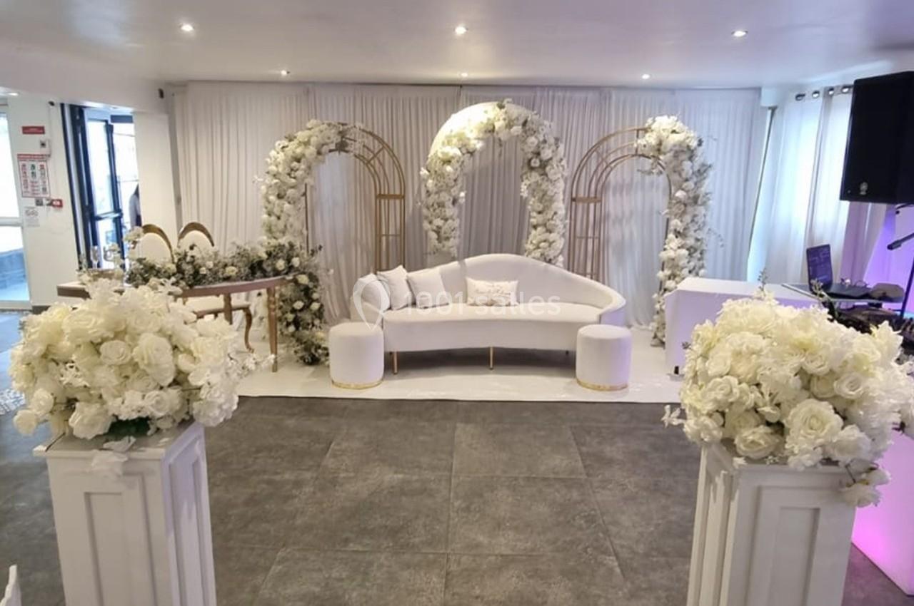 Décoration de salle avec arche florale blanche, canapé et colonnes ornées de fleurs pour un événement élégant.