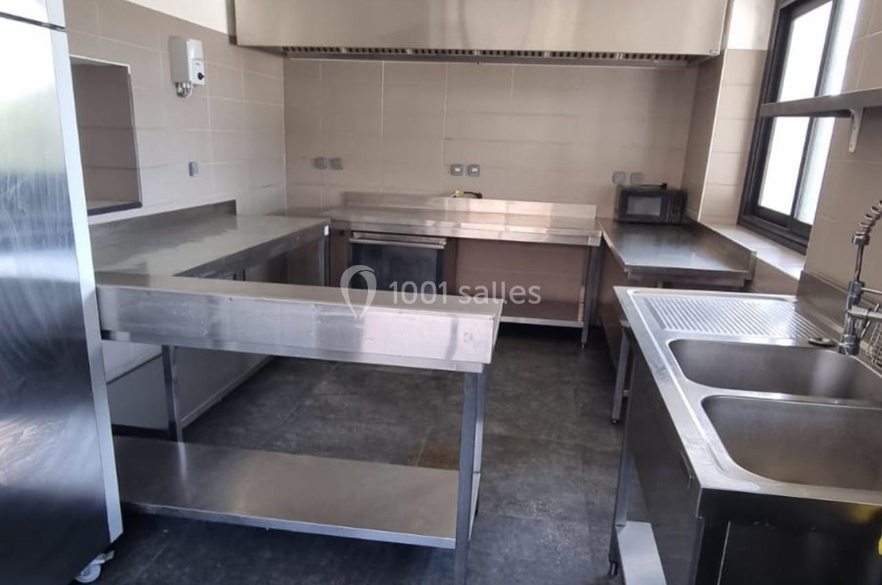 Cuisine professionnelle avec plans de travail en acier inoxydable, évier double et équipements modernes.