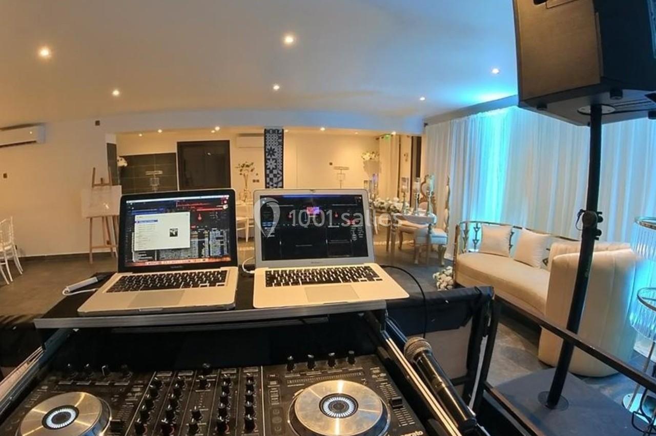 Poste de DJ avec deux ordinateurs portables et une table de mixage dans une salle lumineuse aménagée pour un événement.