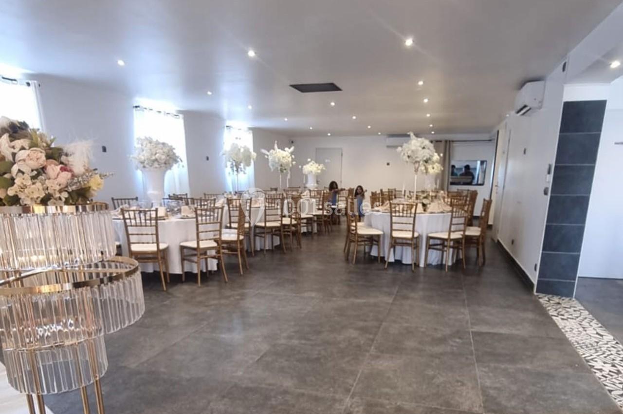 Salle de réception lumineuse avec tables rondes décorées de fleurs blanches et chaises dorées.