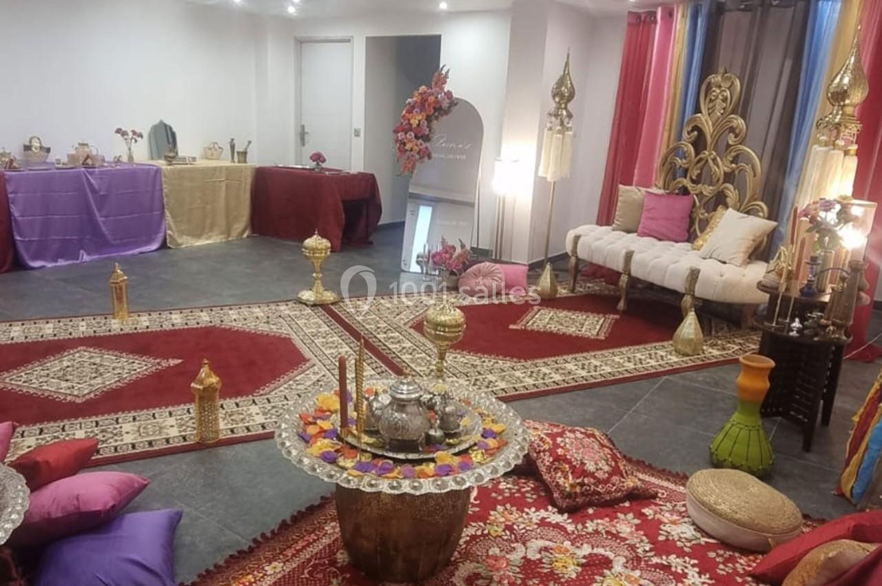 Salle décorée dans un style oriental avec tapis, coussins, lanternes et objets dorés sur un sol en carrelage gris.