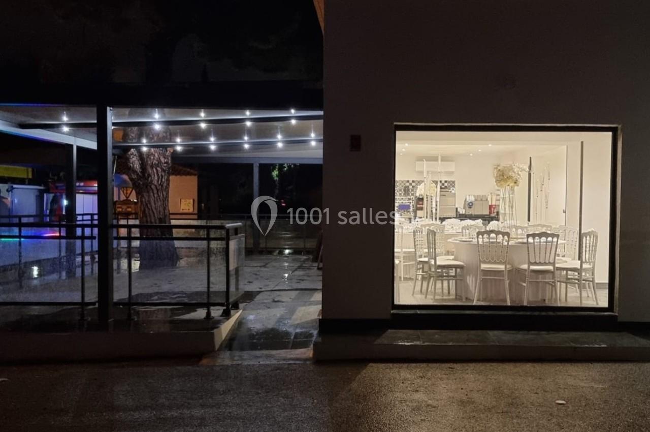 Salle de réception éclairée vue de nuit, avec une terrasse extérieure partiellement couverte et illuminée.