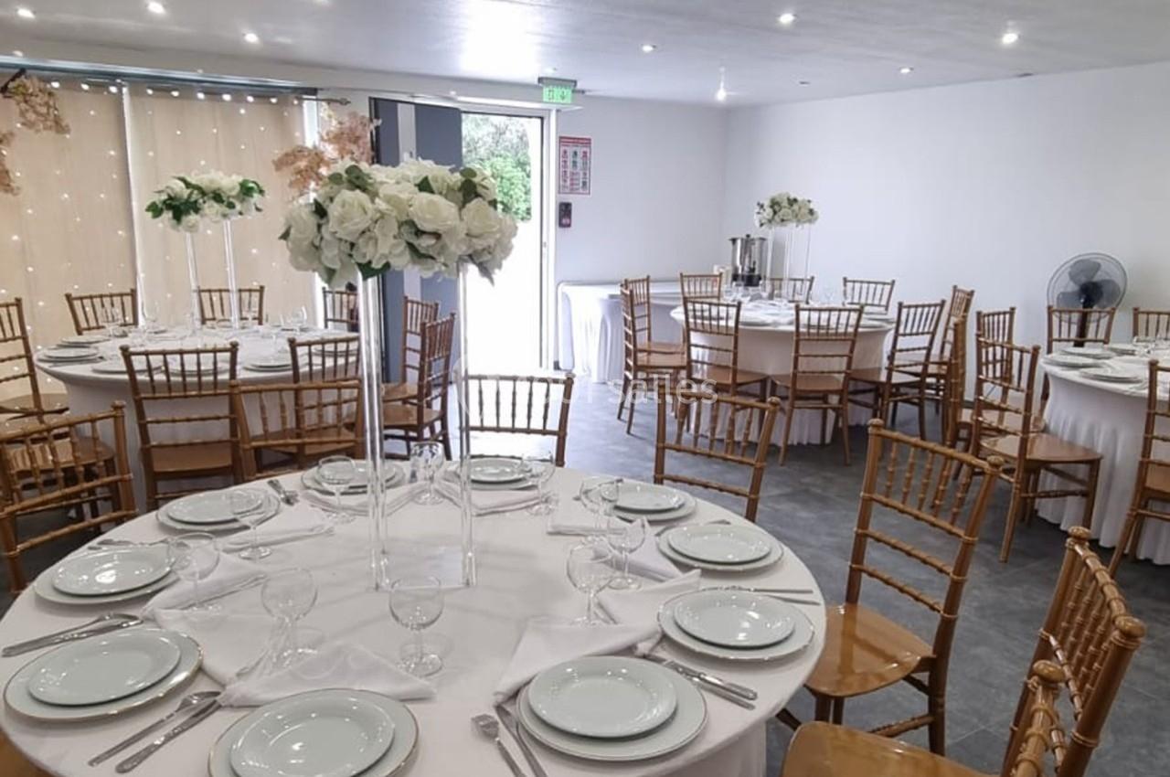 Salle de réception décorée avec des tables rondes dressées, nappes blanches et centres de table floraux.