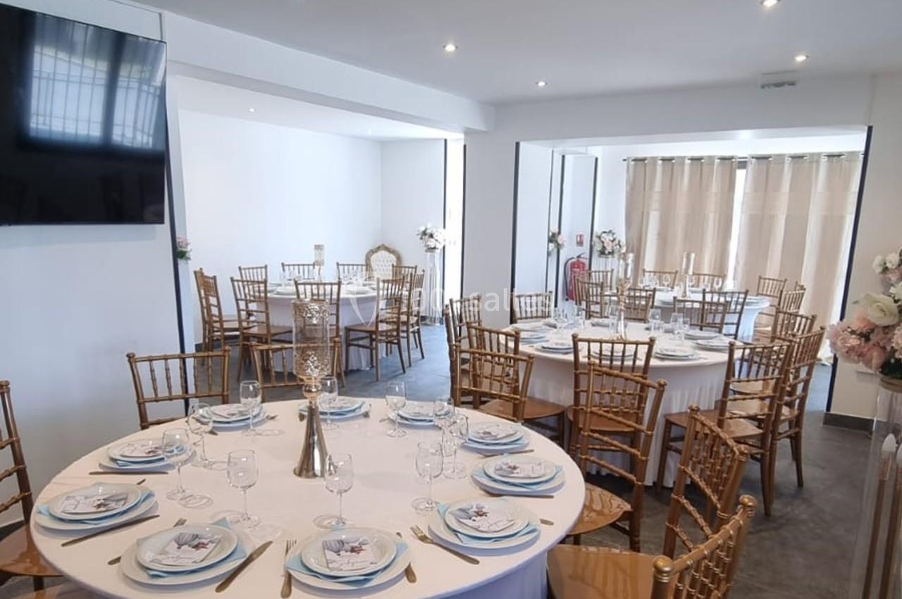 Salle de réception lumineuse avec tables rondes dressées, chaises dorées et décoration élégante.