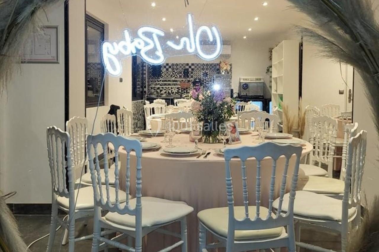 Table ronde élégamment dressée avec des chaises blanches, décorations florales et éclairage chaleureux dans une salle de…