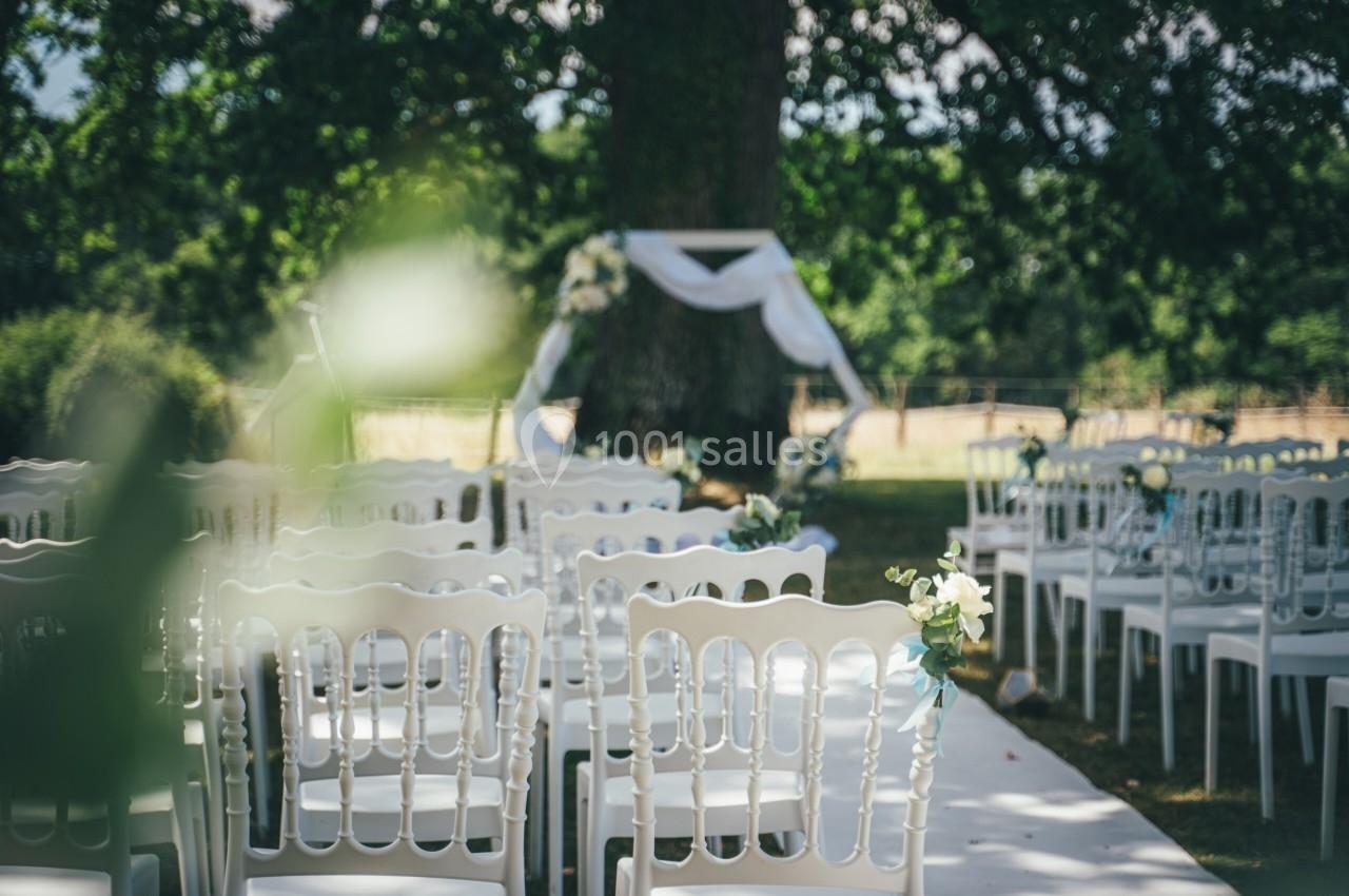 Chaises blanches disposées en rangées face à une arche décorée, dans un cadre extérieur ombragé.