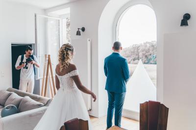 Salle de réception élégante avec tables dressées, chaises blanches et décorations florales sous un éclairage chaleureux.