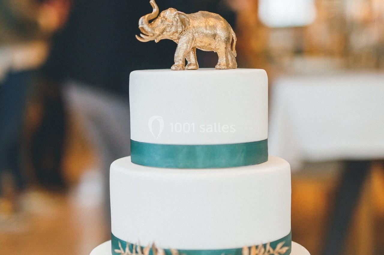 Gâteau à trois étages décoré d'un ruban vert et surmonté d'une figurine d'éléphant doré.