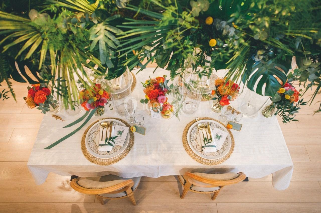 Table élégamment dressée avec vaisselle dorée, serviettes décorées et arrangements floraux colorés sous des feuillages…