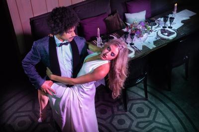 Salle de réception élégante avec tables dressées, chaises blanches et décorations florales sous un éclairage chaleureux.